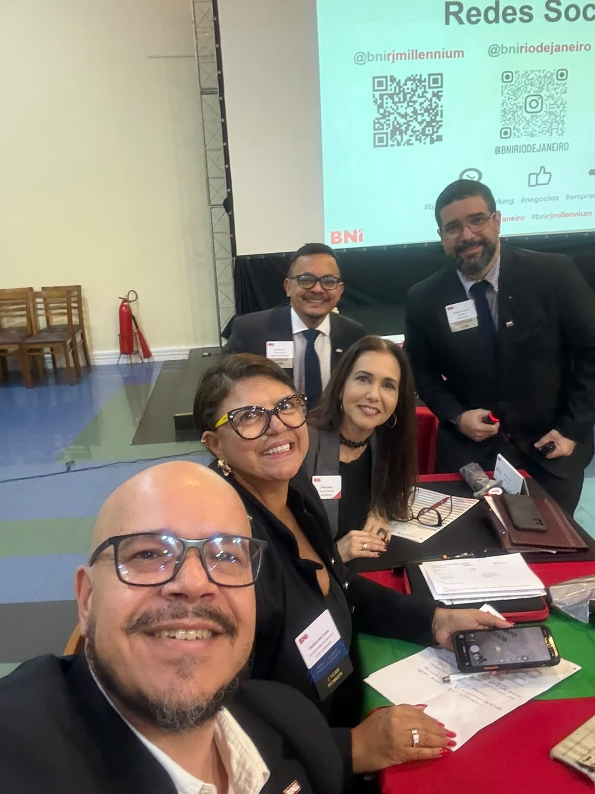 Grupo reunido à mesa, com a tela da reunião ao fundo.