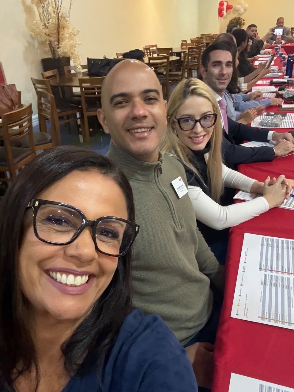 Participantes sentados lado a lado à mesa vermelha.